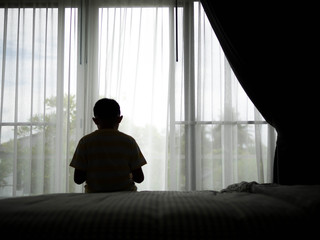 Young boy sitting sad on the bed in the bedroom.