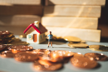 Miniature people, boy standing at home around stack coins using as family and education concept