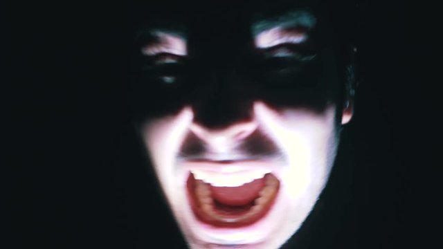 Nightmare shot of a demon face in the darkness moving around screaming and being scary while a light flashes on his face to add drama to the scene