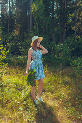 Young girl in a dress and a straw hat on vacation in a forest glade, the concept of relaxation in the countryside in a summer village