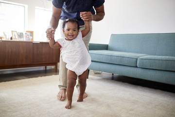 Father Encouraging Baby Daughter To Take First Steps At Home