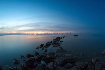 Long row of the stone breakwaters in the calm water of sea bay.