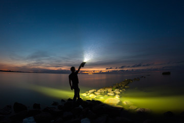 A young man staying on the stone breakwater line and holding very powerful torch.