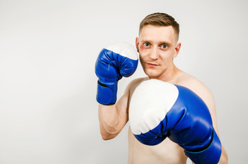 Young man in blue boxing gloves on a light background.