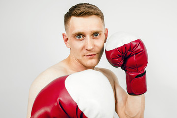 Young guy in red boxing gloves on a light background. Looks forward.