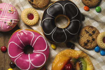 Obraz na płótnie Canvas Round donuts, cookies, and fruitcake, flat lay dessert on wooden table decorate with candy