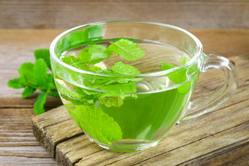 Fresh organic mint tea in glass on wooden table.