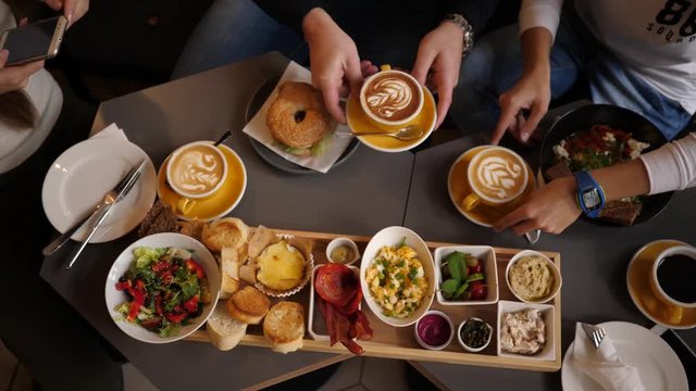 Friends breakfast eating in snack bar - top view on brunch layout with food and coffee cups