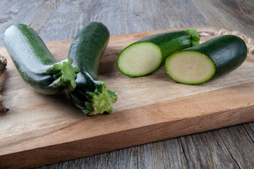 Two Courgettes on a wooden chopping board and another cut in half