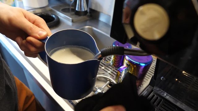 Barista hands hold whisking the milk making cappuccino drink servicing an order in cafe