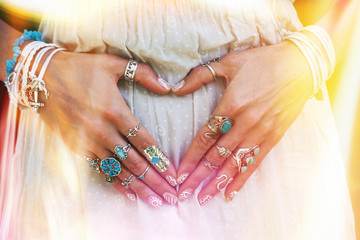 closeup of young woman hands in heart shape with lot of boho style jewrly, rings and bracelets outdoor light leak © Coka