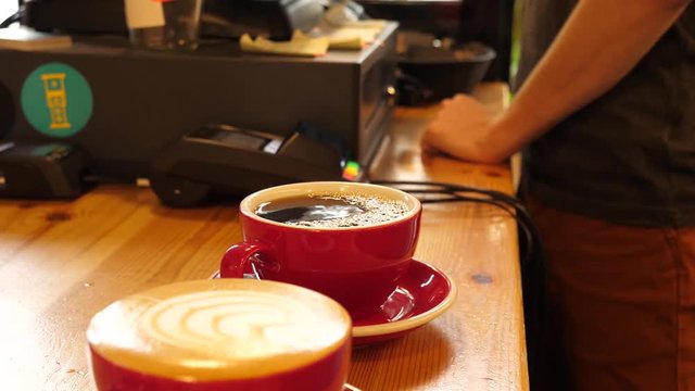 Barista pours cappuccino and classic coffee drink into a cups servicing an order in a cafe