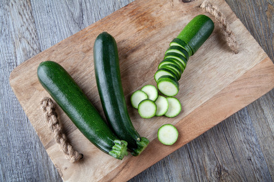Top view ofTwo Courgettes on a wooden chopping board and another sliced courgette