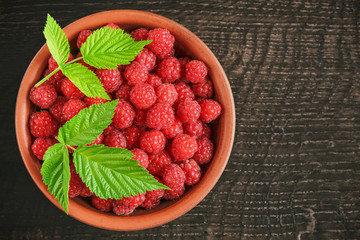 Many berries of red raspberries in a clay bowl on a rustic wooden table