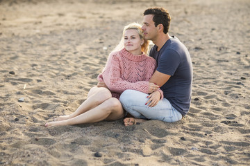 Fototapeta premium nice couple in relationship sitting down on the beach in vacation. sweetness with caucasian young man and woman. blonde and white skin enjoy the love and the age. summer concept
