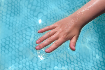 Hand of a teenage girl over water in a close-up pool, concept of water recreation and entertainment