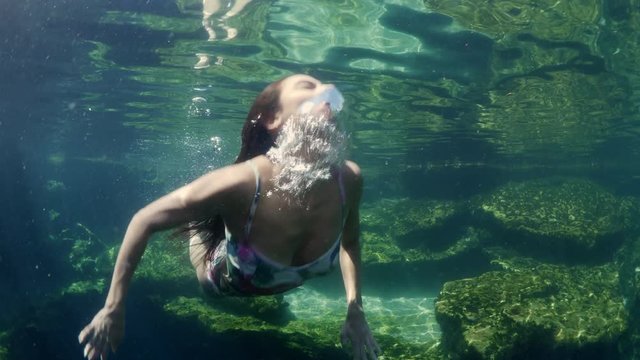 Underwater view of woman approaching then surfacing in natural pool / Meadow, Utah, United States