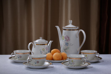 White porcelain tea set with flowers and plate with apricots on a tablecloth