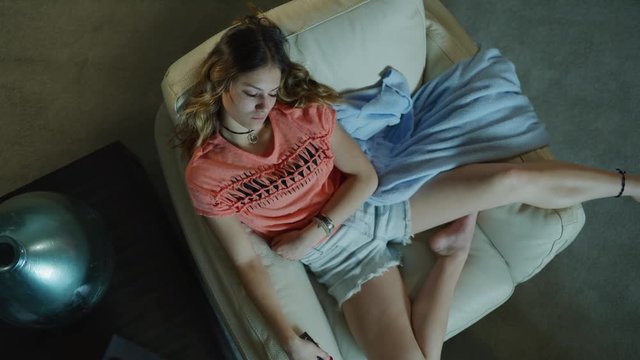 Crane shot of bored teenage girl sitting in armchair watching television / Cedar Hills, Utah, United States