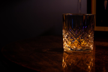 Whiskey being poured into a crystal glass on a dark grained table