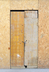 Provisional wooden door closed with padlock. Oriented strand board OSB.
