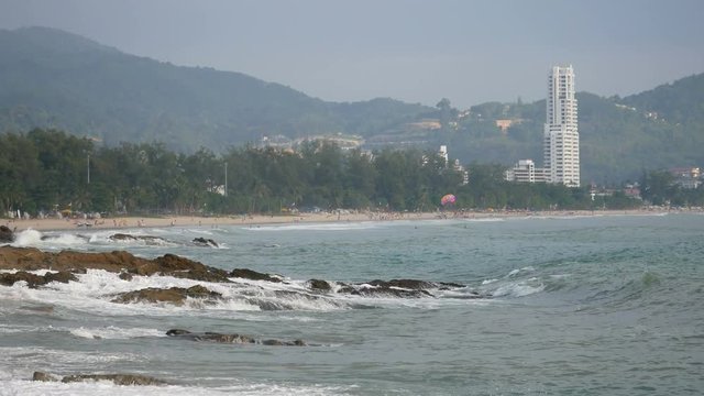 sea wave hit the rock shore seascape , Patong sand beach Phuket  parasail , high building, tree and mountain are  background ,