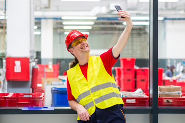 Worker in reflective west with red helmet taking selfie in a factory