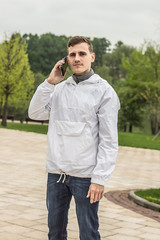Мужчина в светлой куртке говорит по телефону в парке