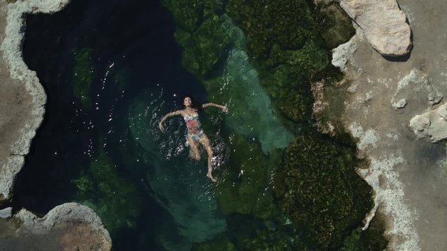 Aerial zoom out view of woman floating in natural pool / Meadow, Utah, United States