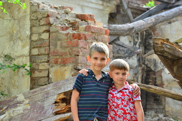 Two brothers stand in an embrace, orphans are left without housing and stand near the ruins of the building as a result of a military conflict, a fire and an earthquake. Photo production.