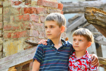 Two brothers stand in an embrace, orphans are left without housing and stand near the ruins of the...