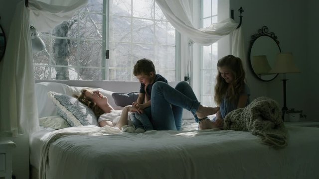 Slow motion of children tickling and playing with mother on bed near bay window / Pleasant Grove, Utah, United States