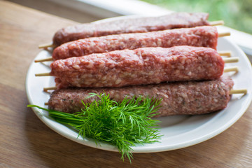 Raw lulya kebab from meat on a white plate with with dill and green onions.