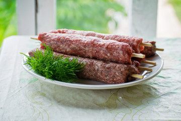 Raw lulya kebab from meat on a white plate with with dill and green onions.
