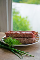 Raw lulya kebab from meat on a white plate with with dill and green onions.