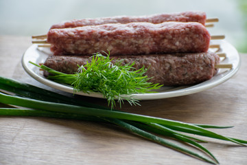 Raw lulya kebab from meat on a white plate with with dill and green onions.