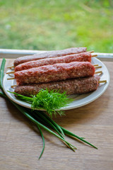 Raw lulya kebab from meat on a white plate with with dill and green onions.