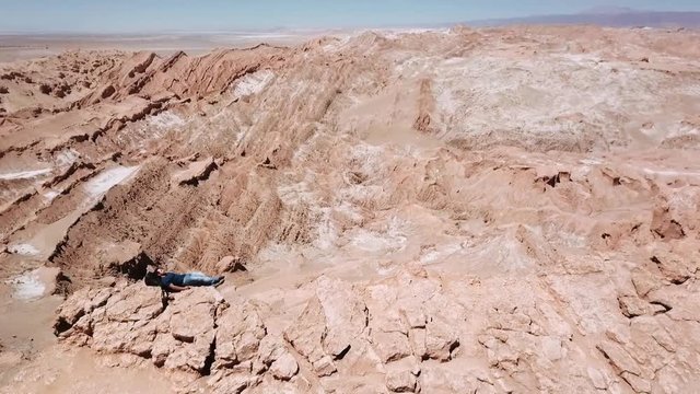 Aerial shot of male trekker resting over the backpack at the cliff's edge in the Atacama desert. 4k