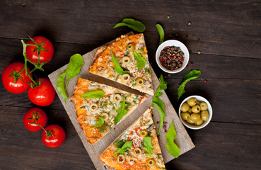 Pieces of pizza with ham, mushrooms and tomatoes on a dark, wooden background. Fast food.