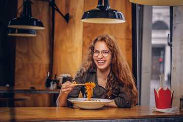 Young redhead female eating spicy noodles in an Asian restaurant. 