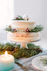 2 tier rustic wedding cake decorated with pine, berries and cotton flower on the wedding table with decor, plates and candles