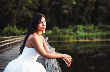 bride in white wedding dress is standing on bridge and posing for camera, wedding day on summer day