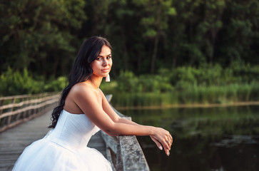 bride in white wedding dress is standing on bridge and posing for camera, wedding day on summer day