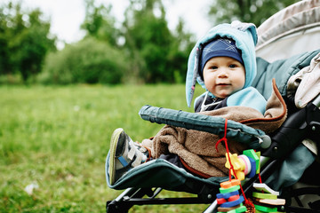 Little baby boy sitting in the stroller at the green garden.