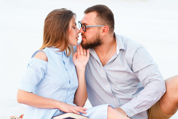 lovely attractive couple sitting together on the white sand beach, looking each other, young couple kissing on the beach, love, romance, loving couple having fun on nature..
