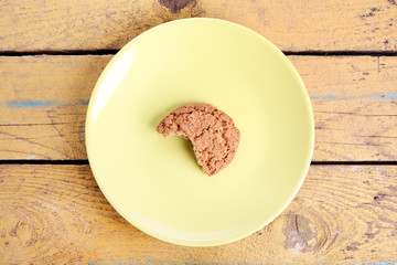 One oatmeal over-baked cookie on a yellow plate, on a wooden yellow background.