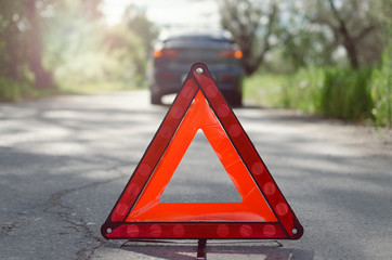 Red triangle emergency stop sign on the road with a broken car behind. Car breakdown concept.