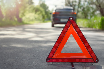 Red triangle emergency stop sign on the road with a broken car behind. Car breakdown concept.
