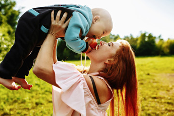 Obraz premium a red-haired woman holds her young son in her arms at sunset in a green Park. They eat an Apple together.