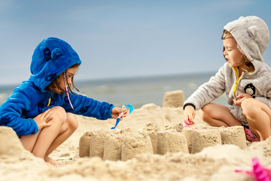two little girls play with dolls in a sand castle on the beach in summer
